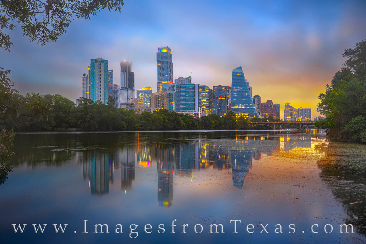 After a night of rains, Lady Bird Lake is calm and smooth. The early morning reflections from the skyline backlit by deep hues...