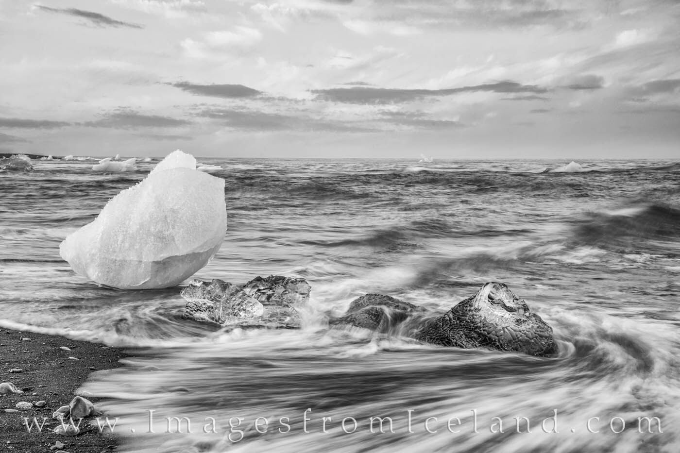 Icebergs drive along the shallow waters of Diamond Beach just outside of Jökulsárlón Lagoon in the twilight of Iceland's long...