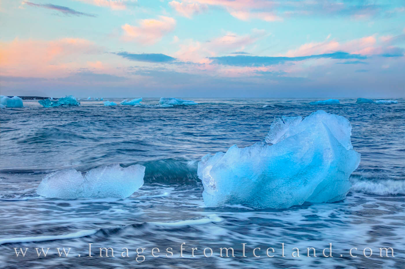 Icebergs float along the black, sandy shores of Diamond Beach in south Iceland beneath the light of midnight in summer.