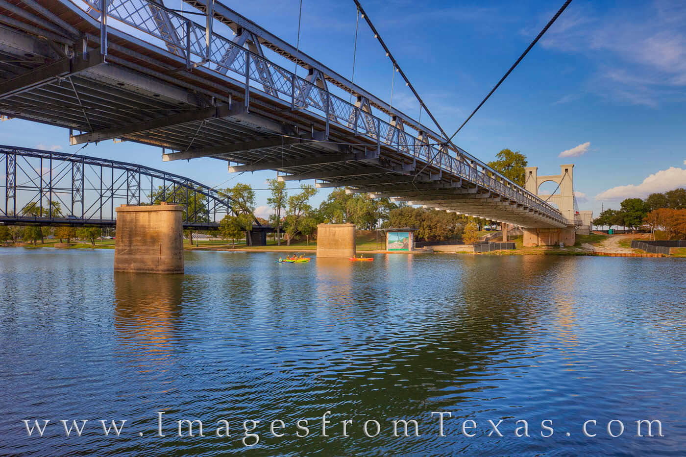Kayakers enjoy a lazy Fall day on the Brazos River in Waco, Texas. Overhead is the well-known Waco Suspension Bridge built in...