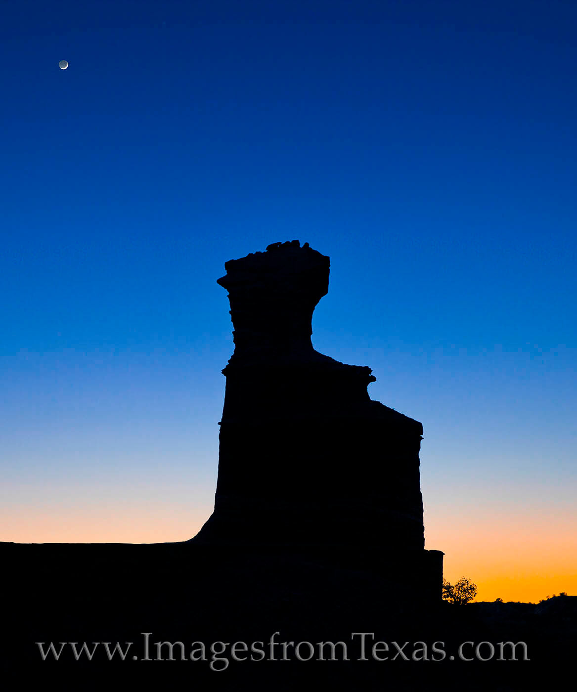 A crescent moon hangs over the Lighthouse in Palo Duro Canyon on a beautiful evening as light quickly fades.