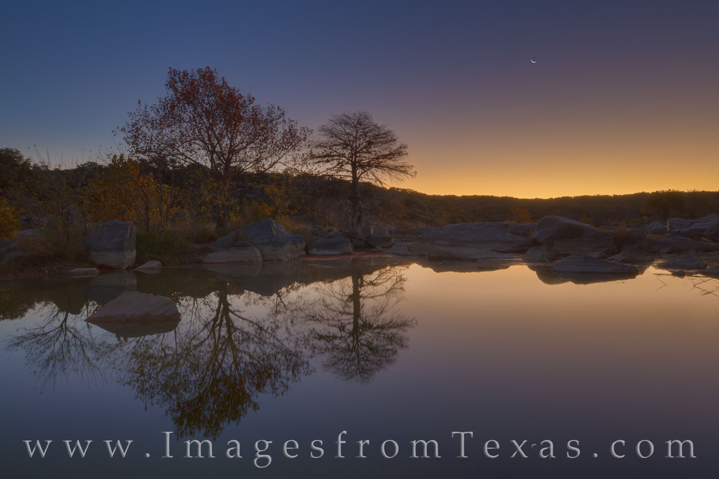The crescent moon rises in the east on an early November morning. A quiet pool in the Texas Hill Country offers a perfect reflection...