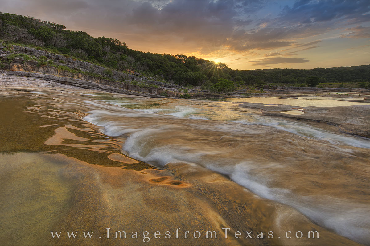 Sunlight peeks over a ridge along the Pedernales River, turning the water and limestone rock a warm shade of orange. Sunrises...