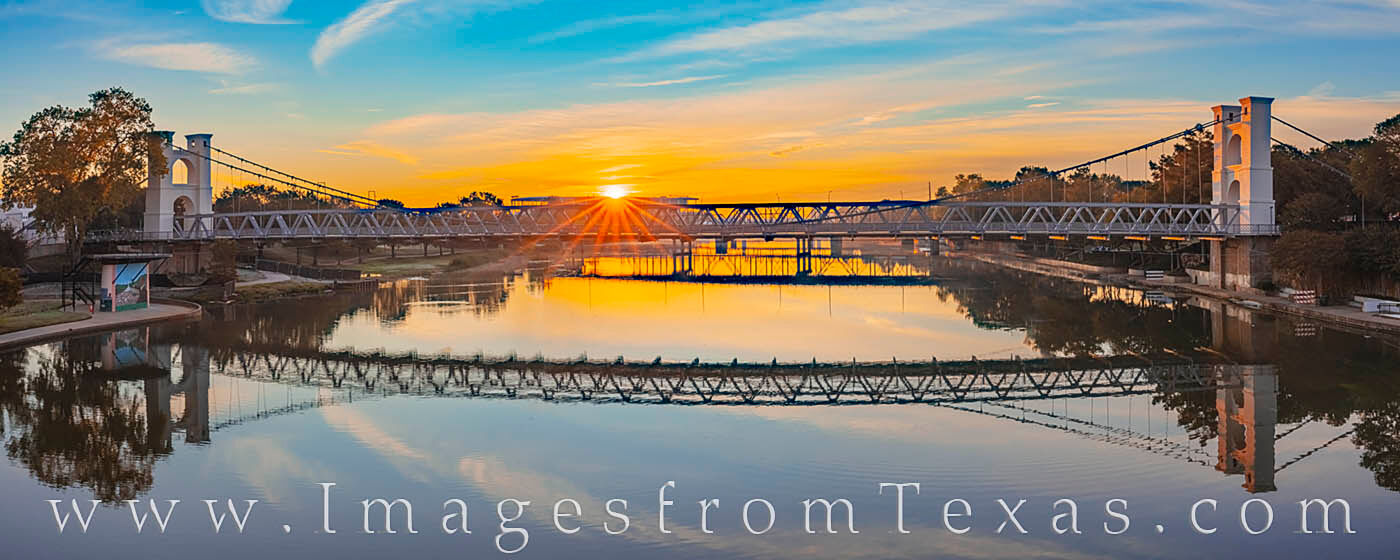 This sunrise panorama on the Brazos River looks across to the Waco Suspension Bridge built in 1869. In the distance, the sun...